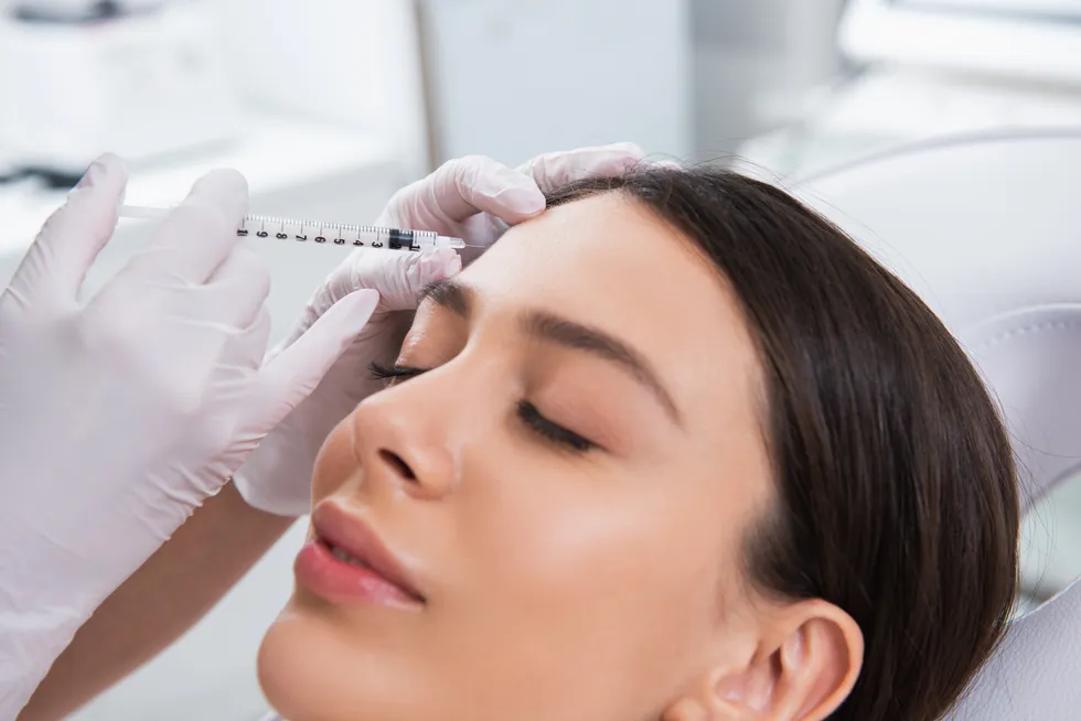 A clinician administering a dermal filler injection to a patient’s forehead