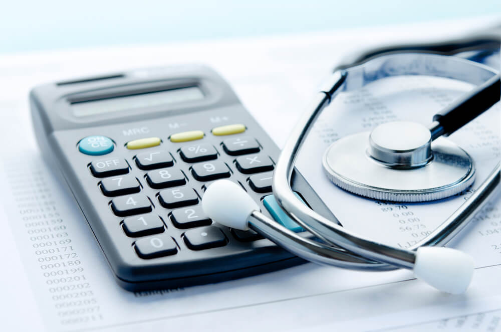A close-up image of a calculator and a stethoscope resting on a financial document. The calculator features a display and buttons for basic calculations, while the stethoscope is silver with a round chest piece. This image symbolizes the intersection of healthcare and finance, highlighting the importance of budgeting and financial management in medical settings.