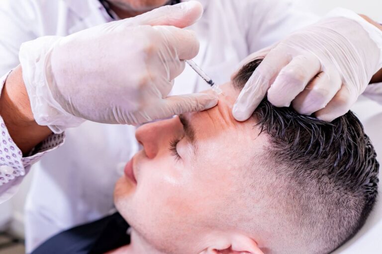 A healthcare professional administers a cosmetic treatment to a male patient, using a syringe to inject a substance into the forehead area. The practitioner wears disposable gloves for hygiene, and the patient appears relaxed with his eyes closed. This image highlights the process of non-surgical aesthetic procedures, often sought for wrinkle reduction and facial rejuvenation.