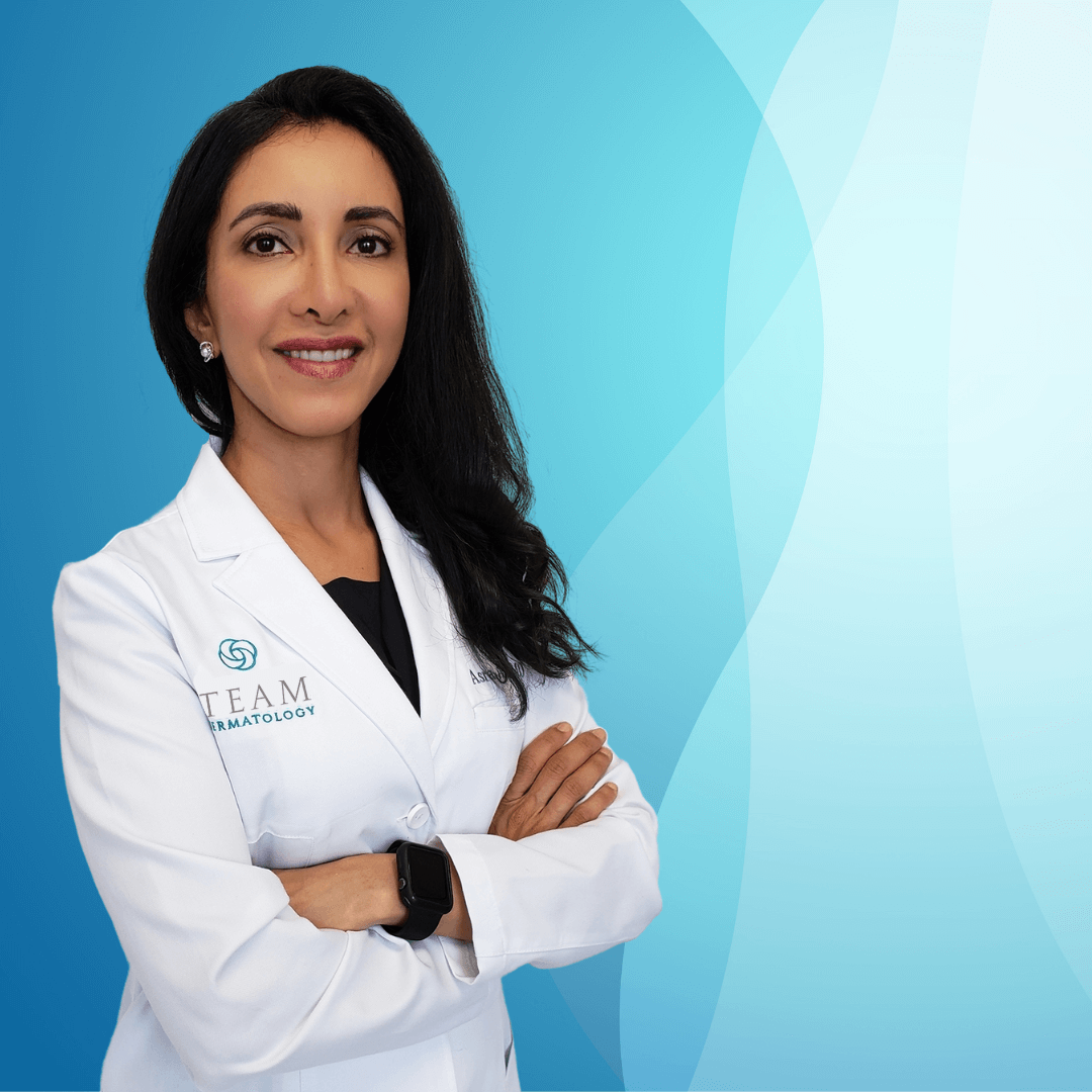 Professional dermatologist in a white lab coat, standing confidently with arms crossed, against a soft blue gradient background. The image conveys expertise and approachability in skincare. Ideal for promoting dermatological services and enhancing online visibility.