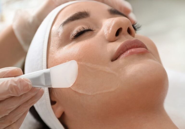 Aesthetician applying a facial treatment to a woman&apos;s face in a spa setting. The woman, wearing a headband, appears relaxed as a soothing gel is applied with a spatula. The image highlights the skincare process, emphasizing self-care and beauty treatments. Ideal for promoting skincare services and highlighting the benefits of professional facial treatments.