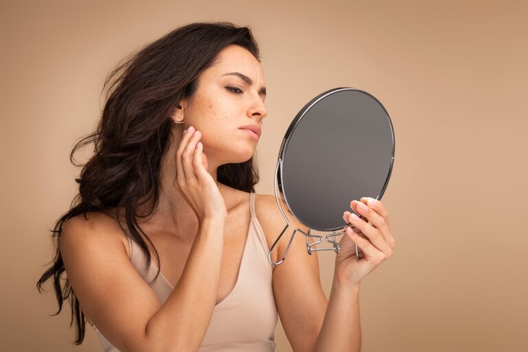 Woman looks at her acne breakout in a handheld mirror.