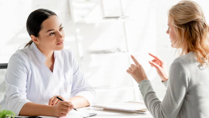 dermatologist sitting at table and listening to patient in clinic